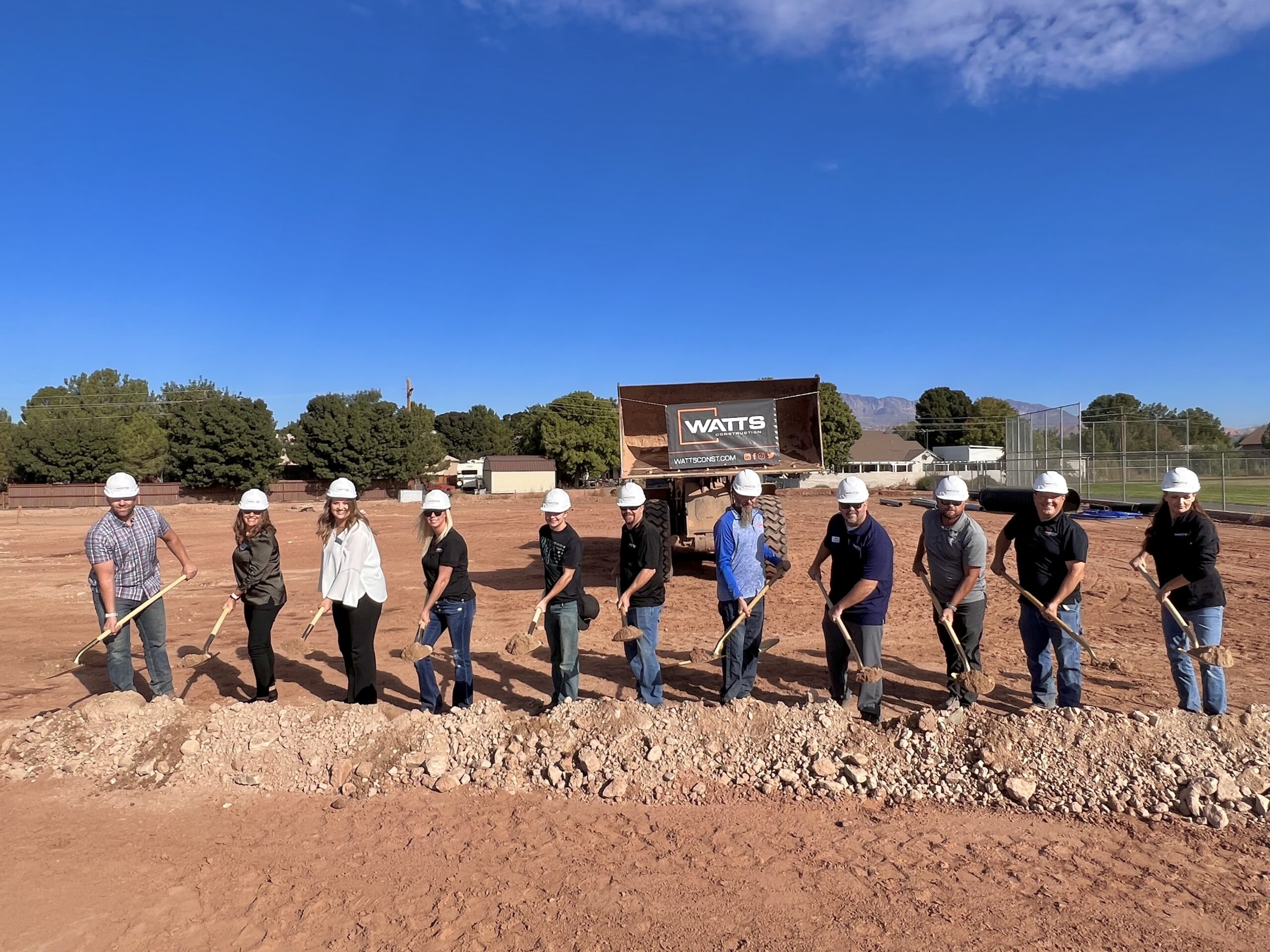 Watts Construction employees pose with gold shovels and turn the dirt